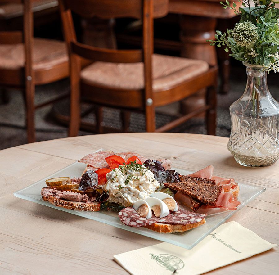 Eine Wurstplatte auf einem Tisch mit einem leeren Stuhl und einer Blumenvase im Hintergrund.